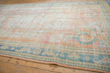 Distressed Oushak carpet close-up, showing faded apricot, blush, and denim blue arabesque patterns.