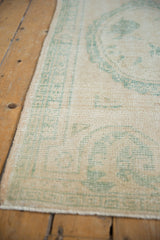 Texture of distressed vintage Oushak runner, showing ivory pile, seafoam green pattern, and side.