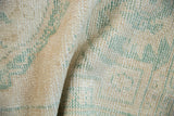 Distressed Oushak rug pile close-up, showing wear, faded ivory, and seafoam green pattern.
