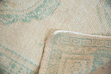 Distressed Oushak rug pile detail, ivory and seafoam green colors, showing worn texture and selvage.