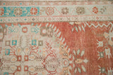 Distressed vintage Oushak rug showing cinnabar red field, faded floral vines, turquoise border, and exposed foundation.
