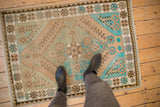 Corner of vintage distressed Oushak rug with geometric floral motifs in turquoise, beige.