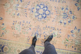 Distressed Oushak carpet with pale apricot field, cobalt floral sprays, visible abrashes.