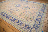 Distressed Oushak carpet corner showing pale apricot field, blue floral sprays, and pronounced abrashes.