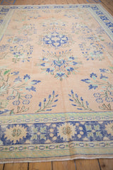 Distressed vintage Oushak carpet, its faded apricot field featuring cobalt blue floral sprays.