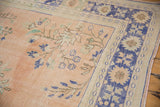 Vintage distressed Oushak carpet showing worn apricot field, cobalt blue border abrashes, and floral motifs.
