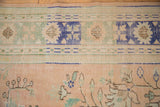 Distressed pale apricot field, seafoam floral sprays, and blue geometric border of vintage Oushak.