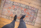 Distressed Oushak runner, brick red, pale blue, ivory, showing worn texture with boots.