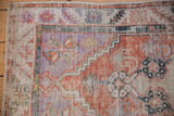 Oushak rug corner shows stepped spandrel, brick red, purple floral motifs, and worn texture.
