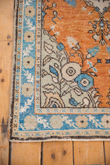 Distressed Oushak rug corner; terra cotta field, sapphire blue border, ivory floral buds.