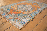 Distressed Oushak rug corner with terra cotta, sapphire blue, ivory floral motifs.