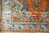 Distressed Oushak rug corner showcases vivid rust, sapphire blue floral details, and aged patina.