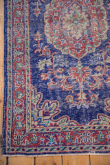 Distressed corner of vintage Oushak rug showing cobalt blue and cherry red vinery with fringe.