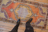 Vintage distressed Oushak rug runner's scalloped medallion and abrashed field in tangerine, saffron, aubergine.