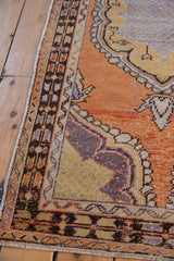 Distressed pile and intact side selvage of a vintage Oushak rug, with tangerine and purple hues.