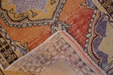 Folded distressed Oushak rug corner with orange, purple pattern and visible hand-knotted reverse.