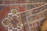 Distressed Oushak rug corner, showing chestnut floral motifs, abrashed pile, and woven foundation.