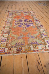 Distressed Oushak rug corner with terracotta, violet, ivory serrated patterns and fringe.