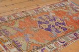 Distressed vintage Oushak rug corner: burnt orange field, violet, pale green spandrel, foundation showing.