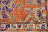 Lower corner of vintage distressed Oushak rug, vibrant geometric border, violet, green, and softened pile.