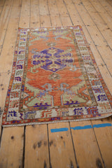 Distressed Oushak rug corner showing violet and orange geometric border with fringe.