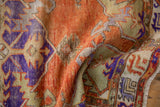 Folded distressed texture of vintage Oushak rug with burnt orange, violet, and pale green motifs.