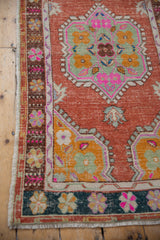 Oushak rug runner corner displaying dark green border with vibrant pink, gold, seafoam floral motifs.