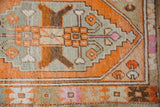 Distressed Oushak rug corner with tangerine, soft green, and brown geometric patterns.