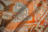 Distressed Oushak rug close-up with tangerine, muted green, beige, and chocolate tones.