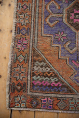 Distressed Oushak rug's side selvage and worn geometric patterns in purple, orange, pink.