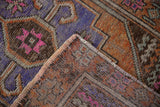Distressed Oushak rug corner showing worn purple, orange, pink pile, hand-knotted reverse, and selvage.