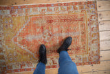 Distressed Oushak rug showing worn pile, brick red, saffron, and pale blue plant motifs.