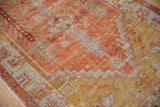 Faded brick red and saffron gold tones of the distressed Oushak rug's zig-zag border and plant designs.