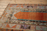 Corner detail of distressed Oushak rug, displaying abrashed orange field and geometric vine pattern borders.