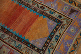 Distressed Oushak rug corner showing geometric floral and vine borders; orange, lavender hues.