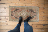 Distressed vintage Oushak rug mat with stepped medallion and person's boots for scale.