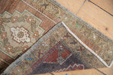 Distressed Oushak rug corner showing hand-knotted reverse with red hues, and textured pile.