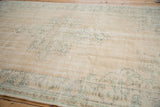 Distressed vintage Oushak carpet detail, showing wear to faded seafoam green motifs on ivory.