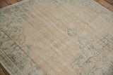 Vintage distressed Oushak carpet shows worn pile, faded ivory, beige, and dusty green patterns.