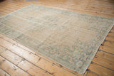 Distressed Oushak carpet's worn pile, highlighting faded seafoam green vine border on an ivory field.