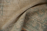 Distressed pile texture of the Oushak rug, revealing faded beige and seafoam green patterns.
