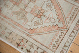 Distressed Oushak rug close-up showing geometric serpent designs, pale rust, and aged ivory texture.