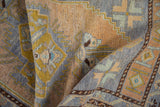 Distressed Oushak rug pile, featuring geometric patterns in pale blue, gold, and beige tones.