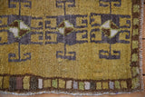 Geometric charcoal rams horn gul on distressed gold green pile with colorful perimeter border.