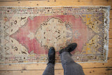 Distressed vintage Oushak runner with an abrashed dusty mauve field and ivory floral medallion.