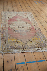 Distressed Oushak rug runner corner, showing faded mauve, ivory, yellow, and blue border.
