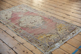 Distressed Oushak rug corner, meandering vine border in mauve, ivory, saffron yellow.