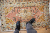Distressed vintage Oushak rug: worn center medallion, dusty sandalwood, saffron, seafoam, with feet.
