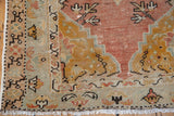 Faded dusty sandalwood, saffron, and seafoam patterns on distressed Oushak rug corner.