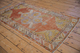 Distressed vintage Oushak rug corner with burnt orange, saffron, and lilac geometric patterns.